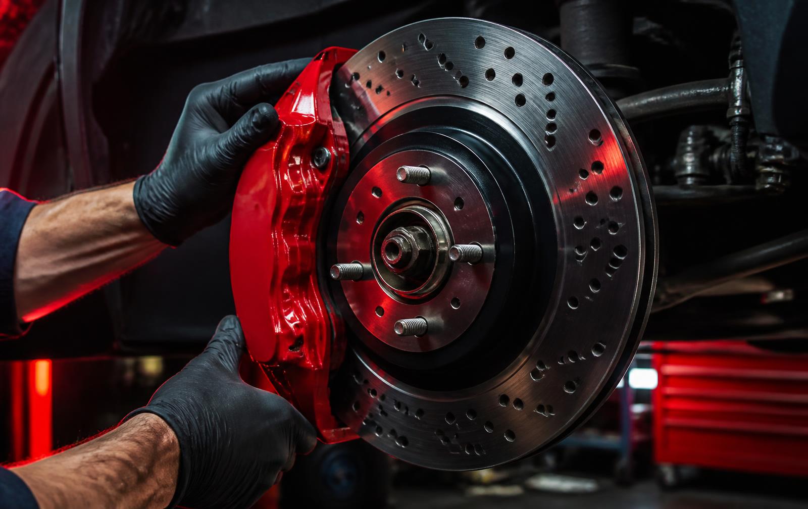 Mechanic fitting a new red brake caliper over a machined rotor